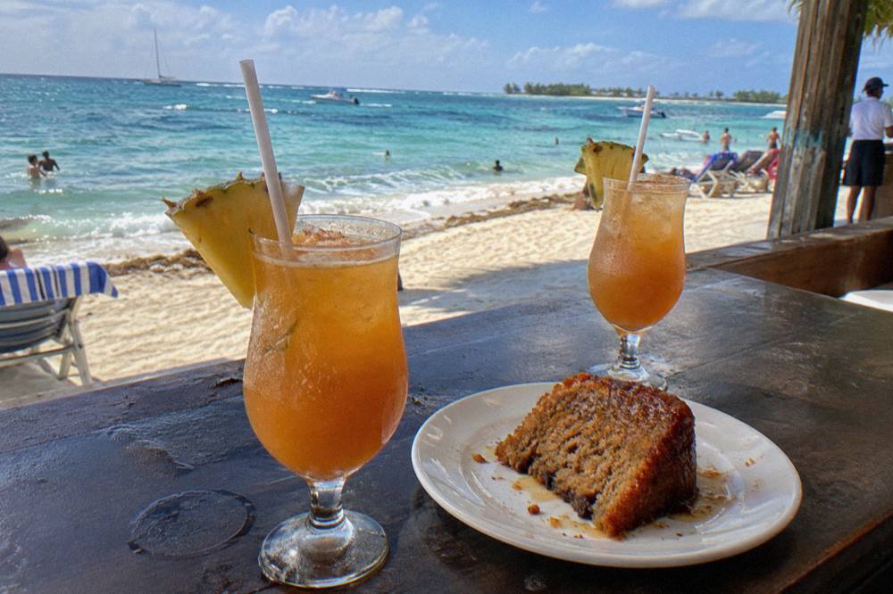 Two amber rum cocktails garnished with pineapple and nutmeg on a weathered waterfront bar top.