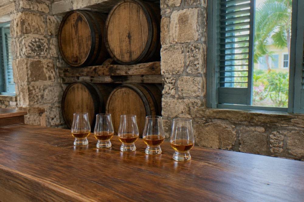 A guide pouring amber rum into tasting glasses for a small group on a distillery veranda.