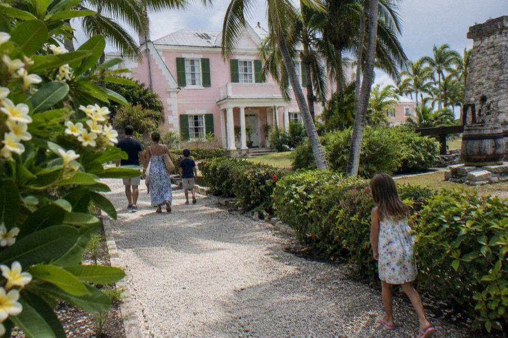 Family group walking through tropical gardens toward a historic pastel estate building