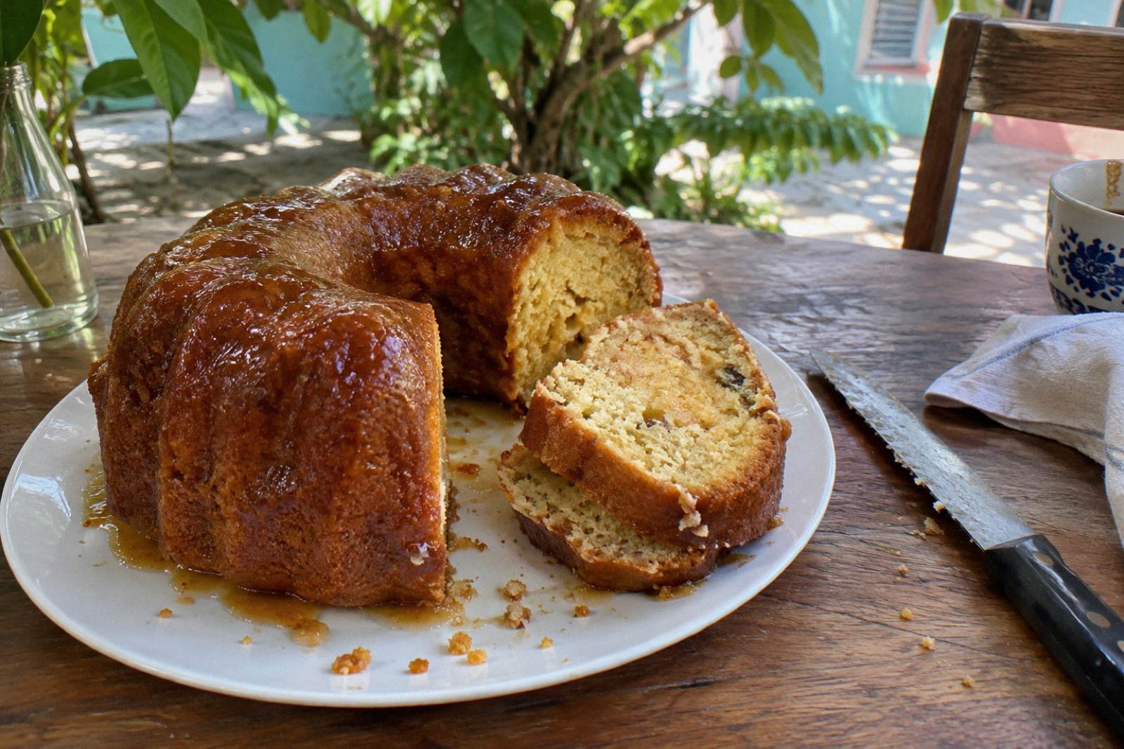 Sliced Bahamian rum cake on a wooden board beside a bottle of amber rum