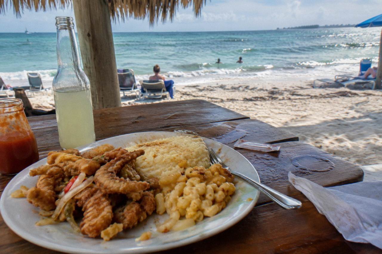Plate of fried conch and sides on a wooden table at an open-air Nassau seafood spot