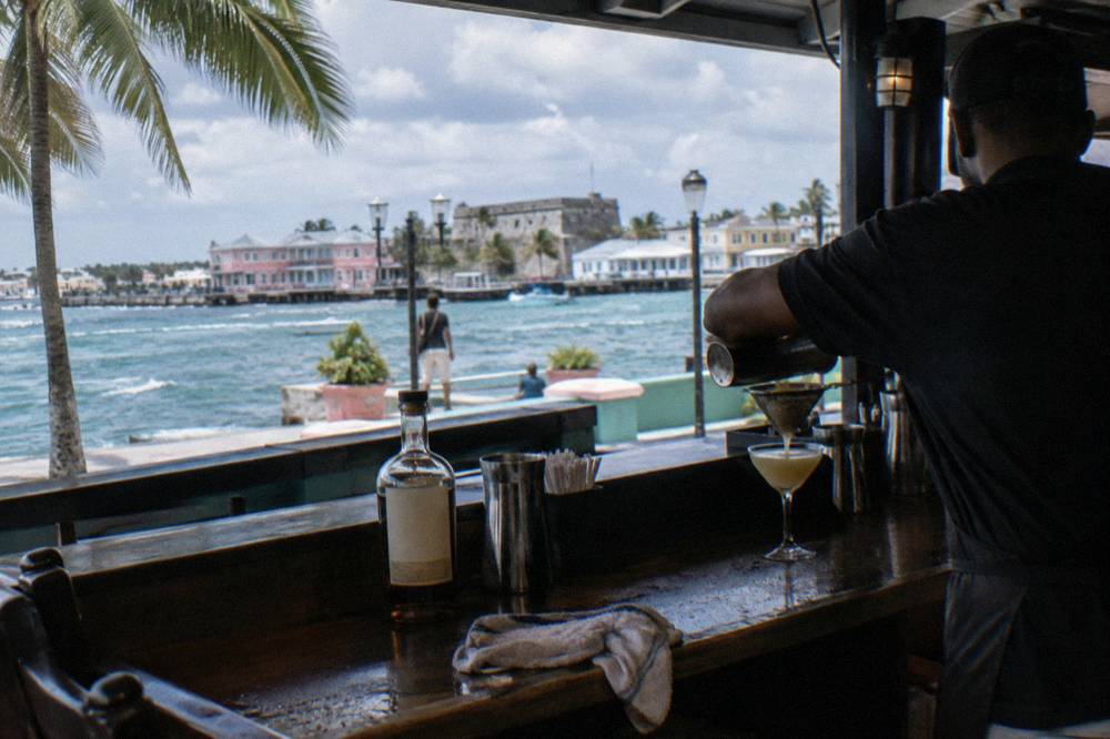A bartender straining a rum cocktail into a glass at a wooden Nassau bar