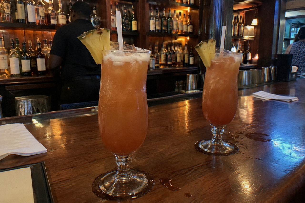 Two rum cocktails garnished with pineapple and nutmeg on a wooden bar top in Nassau