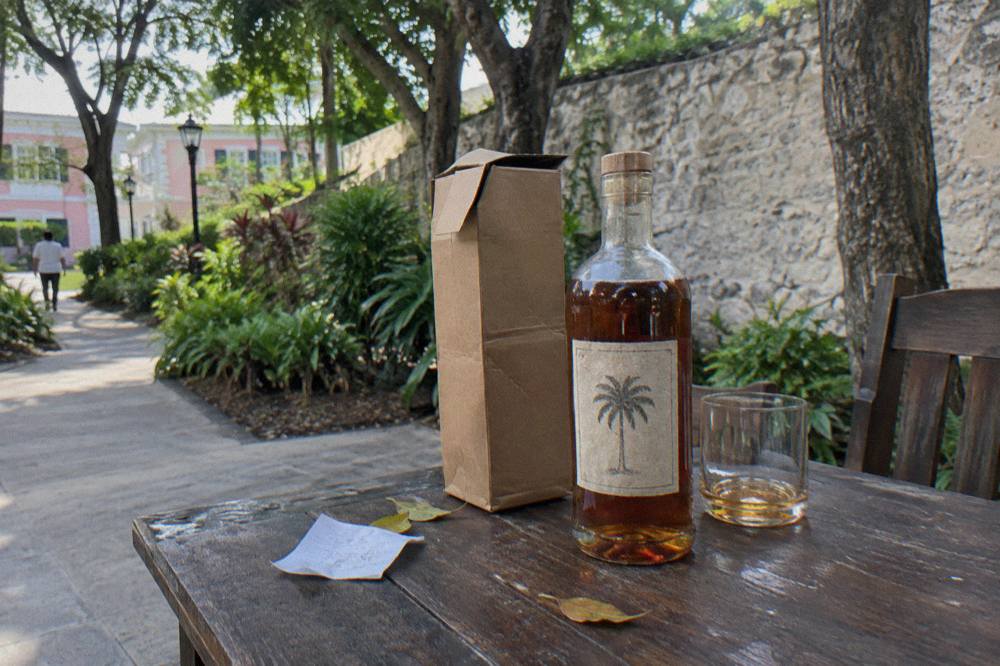 A paper-wrapped rum bottle tucked between folded clothes in an open suitcase