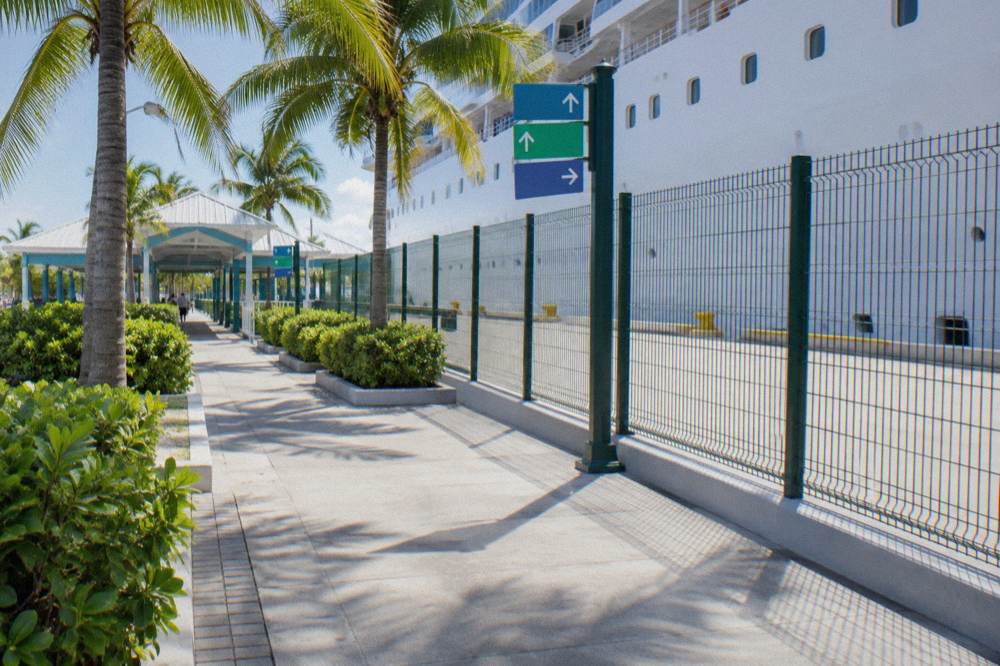 Passengers walking along a waterfront promenade toward a docked cruise ship in late morning light