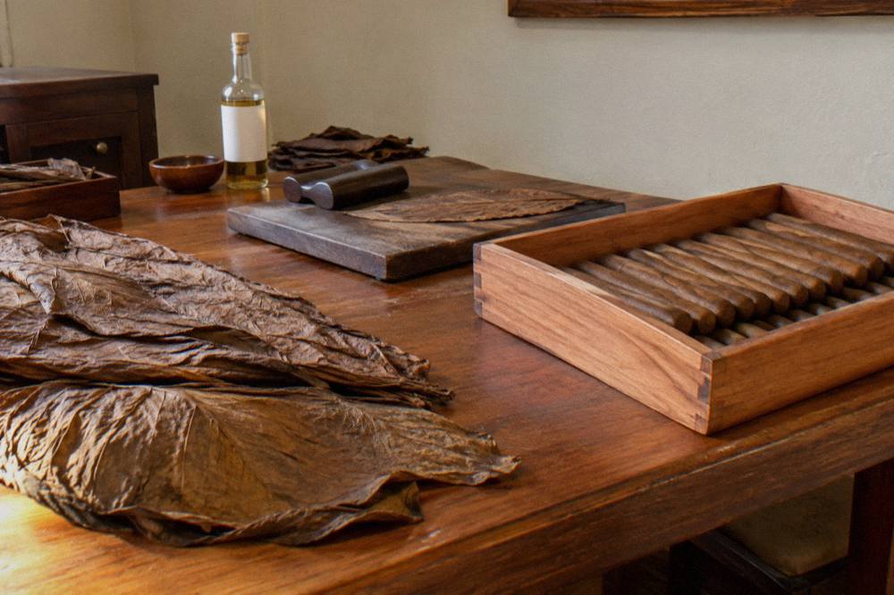 Hands rolling a cigar on a wooden workbench in an open workshop