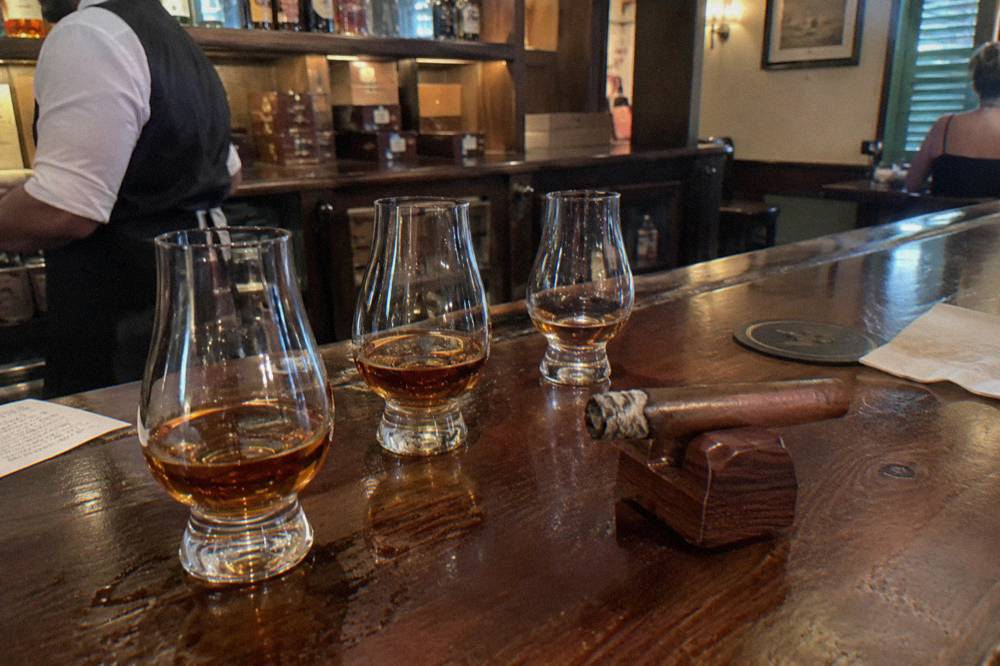 A flight of rum glasses and a rolled cigar resting on a wooden tray
