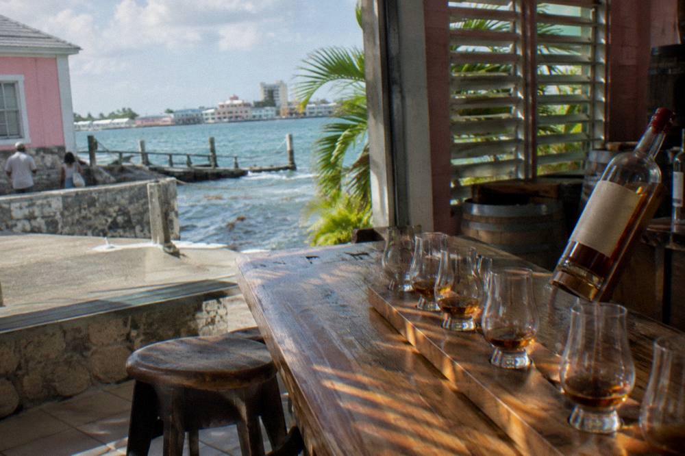 Rum tasting glasses lined up on a wooden bar counter at a Nassau distillery