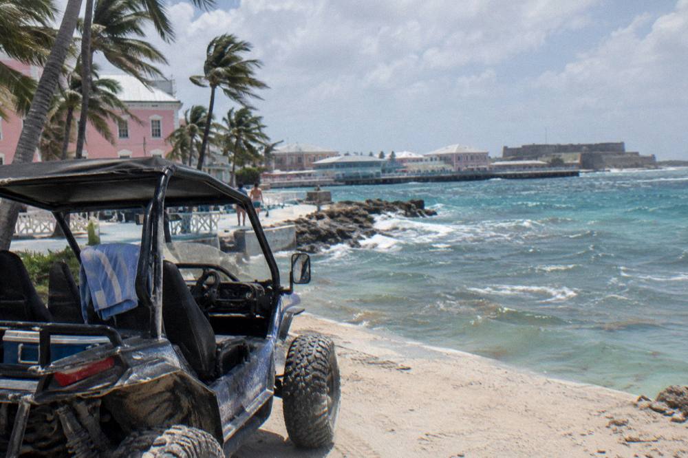 An open-sided buggy vehicle parked on a coastal road under palm trees
