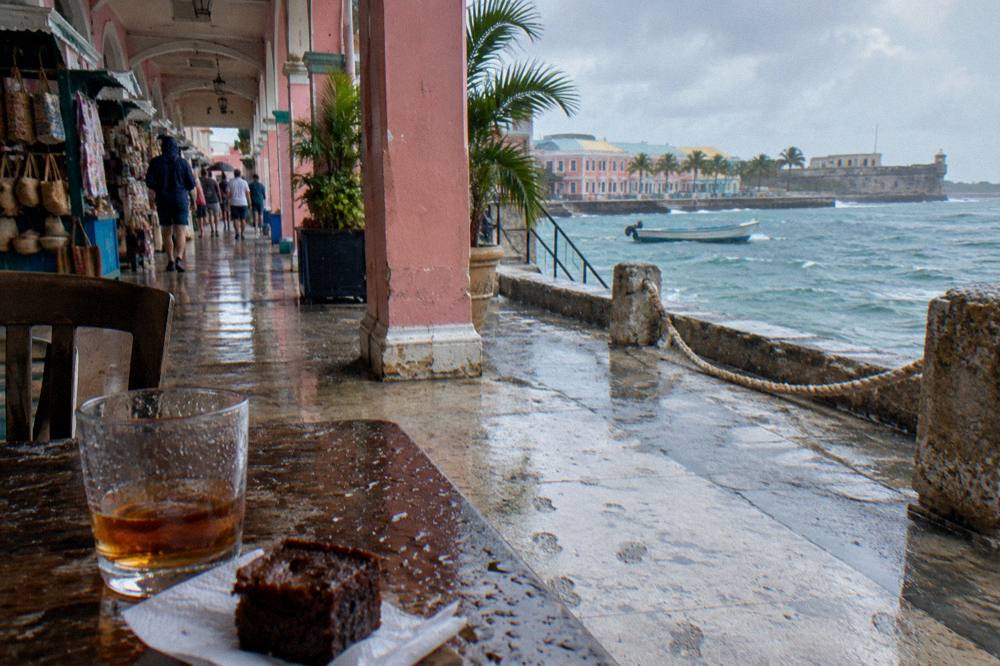 Glass of amber rum beside a small rum cake on a wooden table at a tasting bar