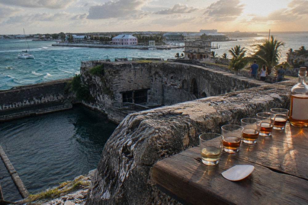 Rum glasses lined up on a wooden bar counter beside an old stone wall