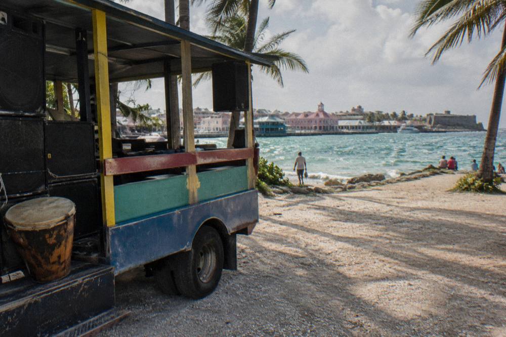 Open-sided party bus with speakers and drums parked under palm trees