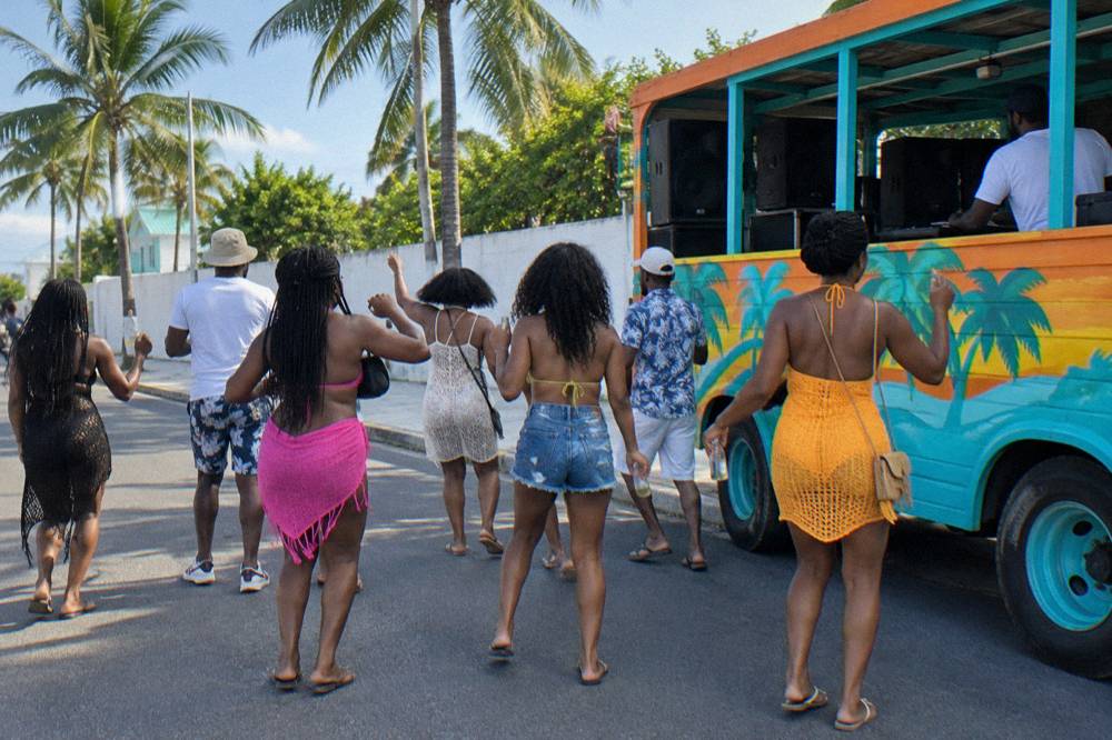 Crowd dancing beside a decorated party bus on a sunny Nassau afternoon