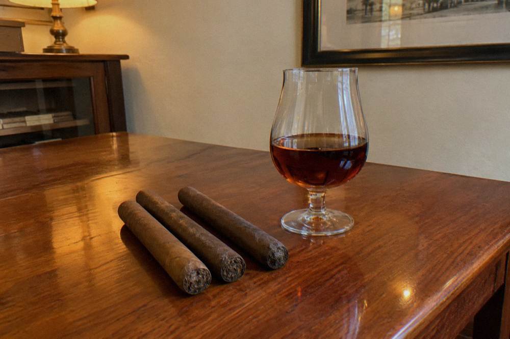 Hand-rolled cigars resting on a cedar rolling table beside a glass of rum