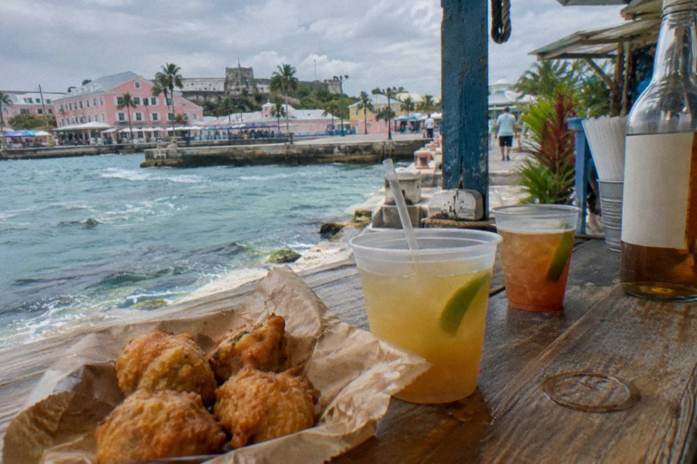 Conch fritters and two rum cocktails arranged on a wooden bar top