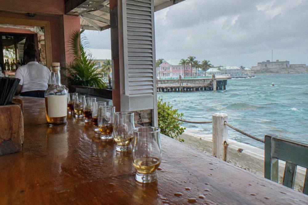 A row of small tasting glasses filled with pale and amber rum on a dark wooden bar top