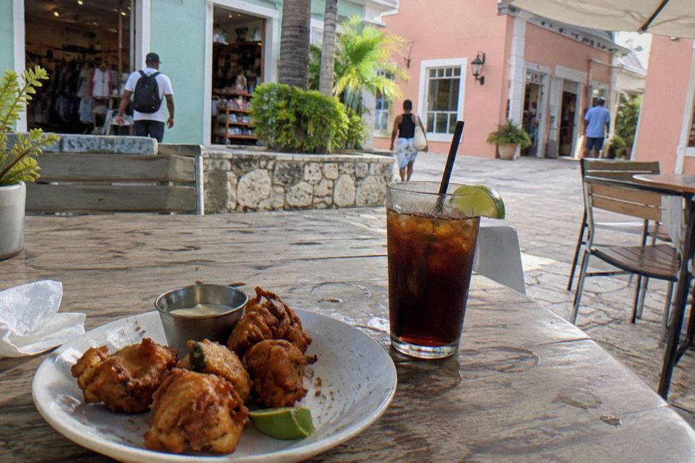 A plate of golden conch fritters beside a rum cocktail on an outdoor table