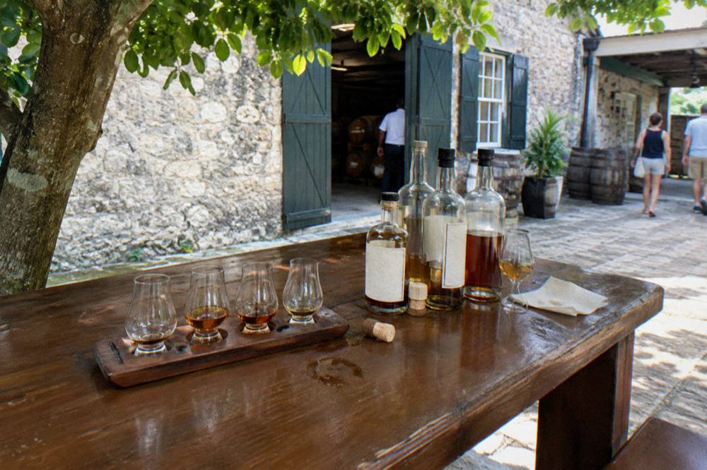 Bottles of rum and a tasting flight arranged on a barrel in a dim distillery storehouse