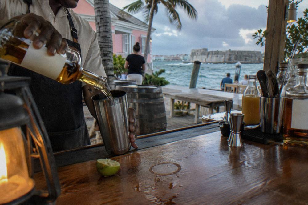 A bartender pouring amber rum into a cocktail shaker on a wooden bar top