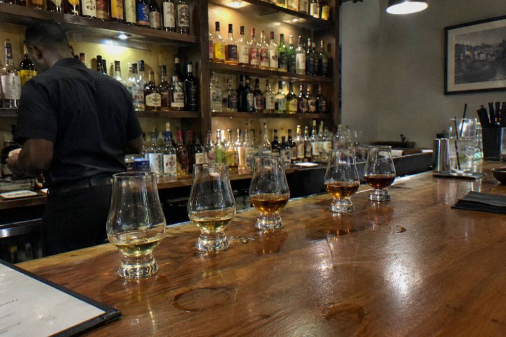 A row of tasting glasses with different colored rums arranged on a barrel top