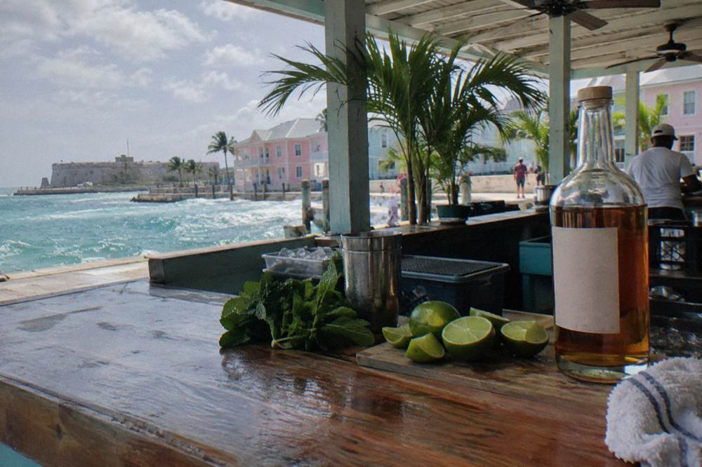 Cocktail ingredients including limes, mint and a bottle of rum arranged on a bar counter