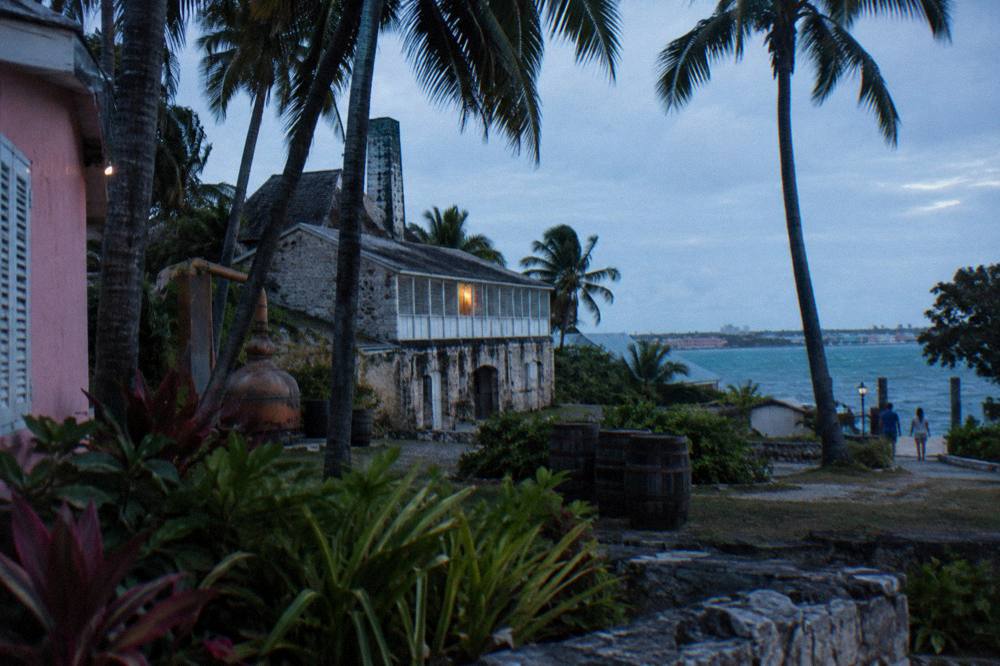 A historic stone distillery building surrounded by tropical gardens in late afternoon light