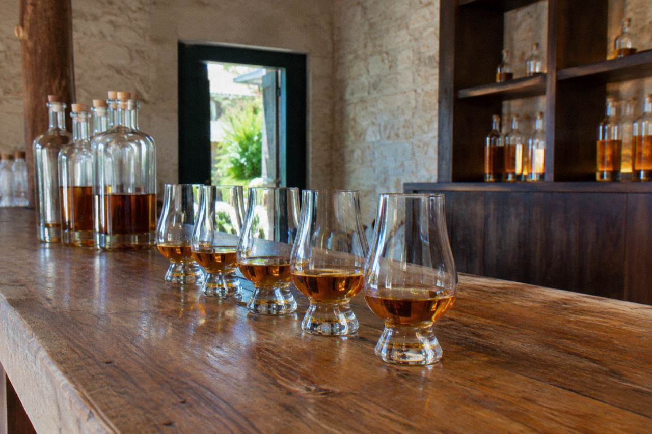 Glasses of amber rum lined up on a wooden tasting bar inside a distillery