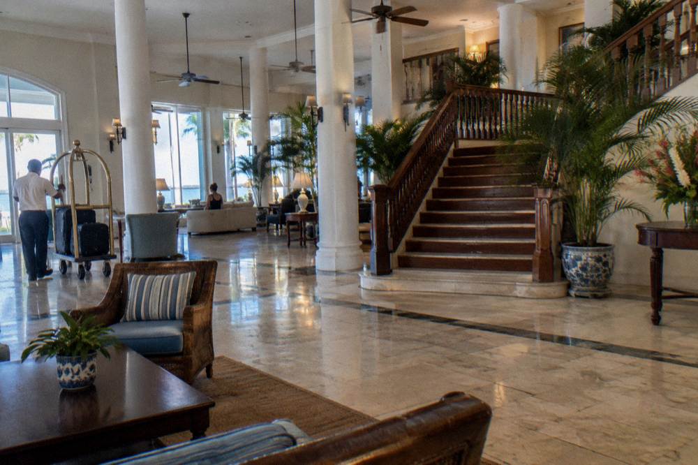 Grand high-ceilinged hotel lobby with white columns, marble floor and a wide wooden staircase in downtown Nassau